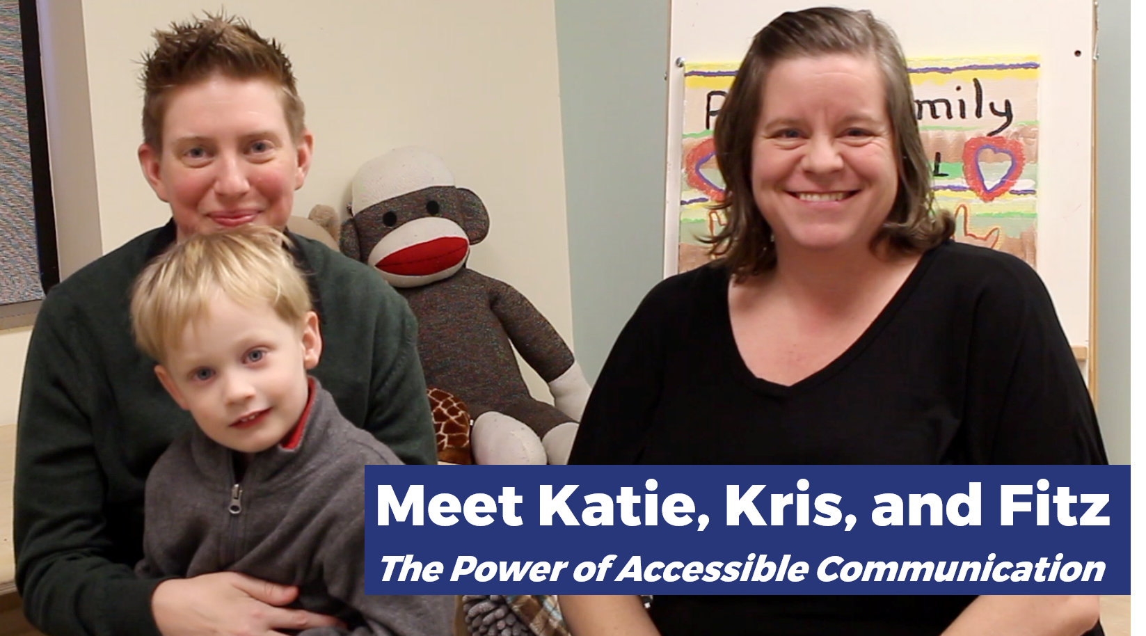 Katie, Kris, and Fitz smiling for the camera. Two adults and one child sitting in a classroom. The adult on the left has short, spiky light brown hair with light skin and a dark gray sweater. They are sitting with the child, who has short, straight blonde hair with a gray sweater. The person on the right has brown hair down to their shoulders and light skin, with a black blouse. In the bottom right, blue bars have the text: "Meet Katie, Kris, and Fitz / The Power of Accessible Communication".